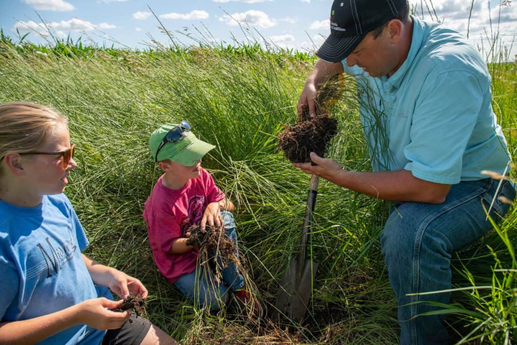 Rancher inspecting grass and soil with kids